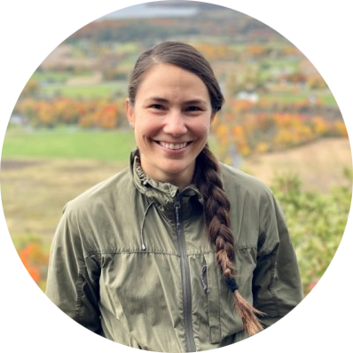 Ariana Cano Gomez: A mid-thirties Latina, hair pulled into a braid at one side, standing wearing a jacket in the outdoors and smiling happily at the camera.