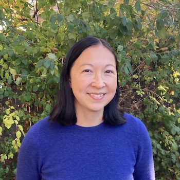 Adrienne Miao: 39 year old Asian-American woman with shoulder length brown hair standing outside with trees in the background..