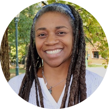 Winnie Looby: a Black woman in her early forties, wearing long locs held back with a headband smiles warmly at the camera