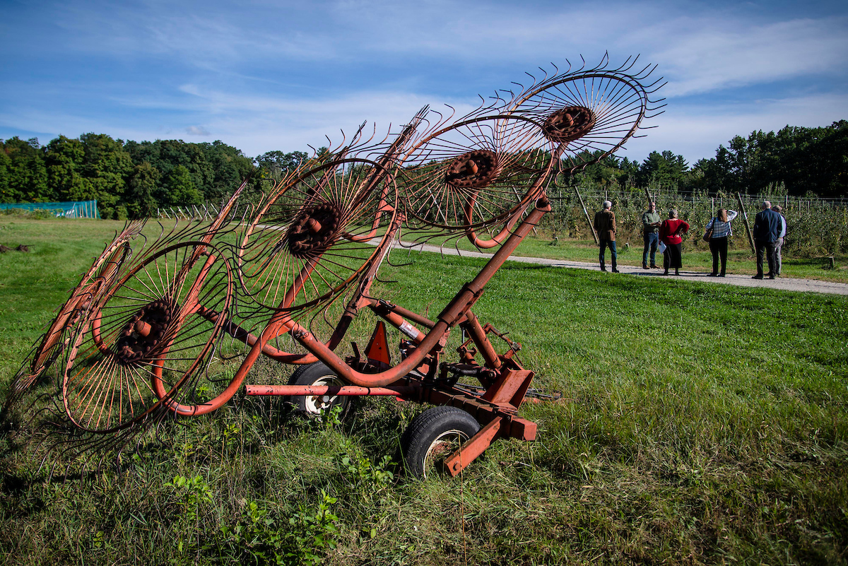 A group of individuals stand on a farm next to some equipment