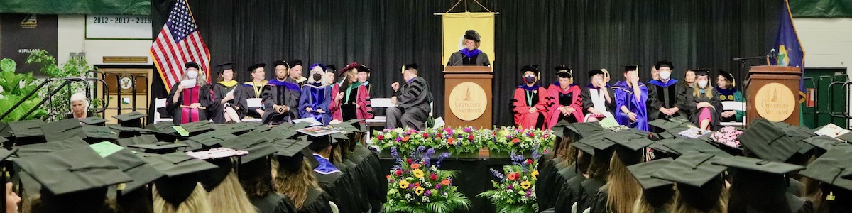 faculty seated on commencement stage wearing regalia with sea of seated graduates in graduation caps in the foreground