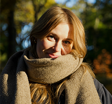 Sarah wrapped in a beige scarf smiling for the camera