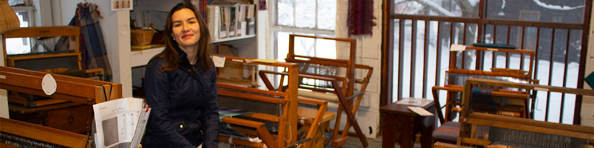Smiling person in a sun filled room with fiber and looms 