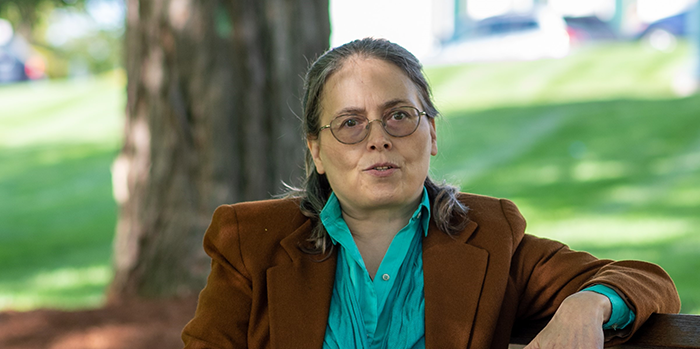 Jeanne Shea seated on a bench shaded by trees on UVM Green