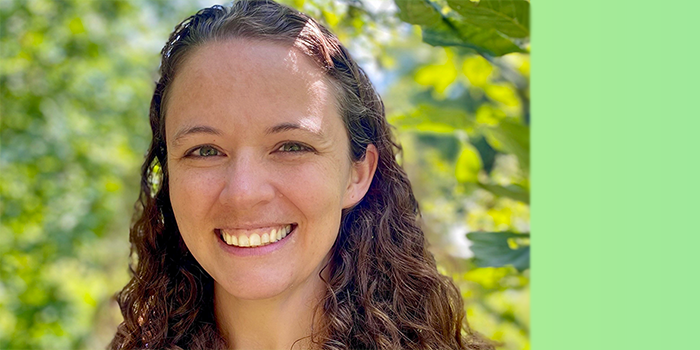 Emily, smiling, in an outdoor setting with greenery in the background