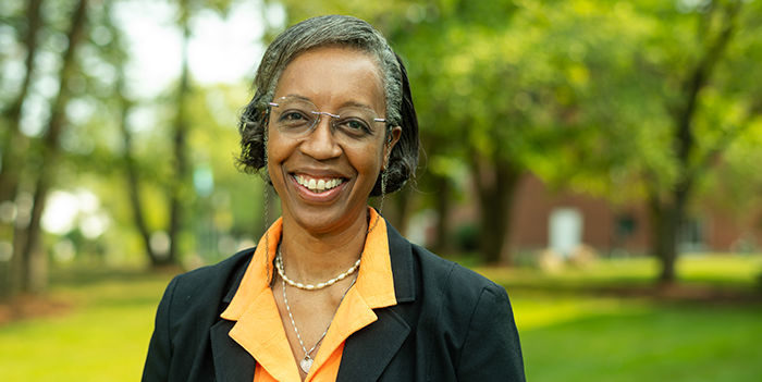 Lesley-Ann smiling broadly with green trees and bushes in the background