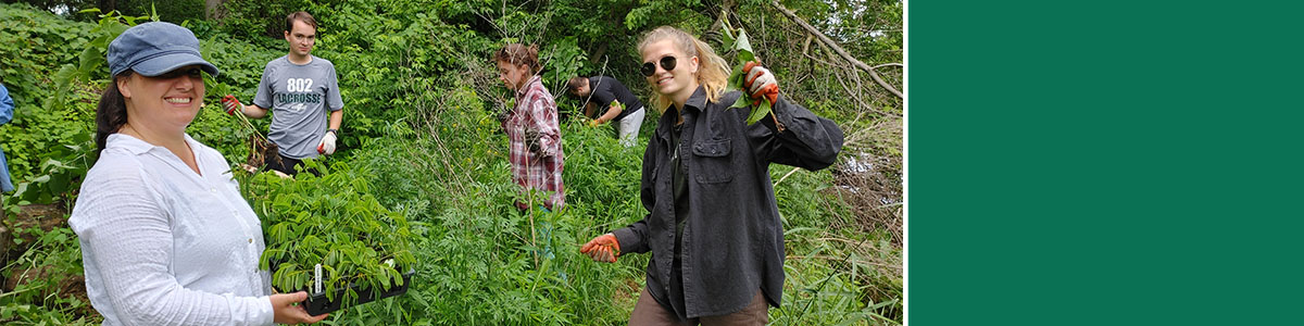 Plant Biology Instructor Laura Hill and students are standing on a river bank replacing invasive plant species with native plants.