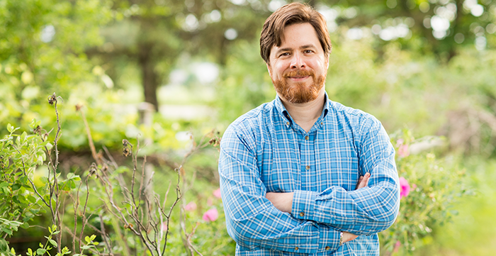 Peter Henne outdoors with wildflowers and trees in bloom behind him