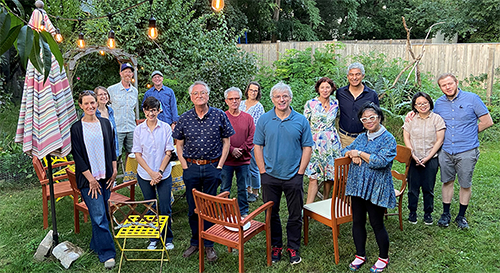 Sociology faculty and staff outdoors with hanging lights, trees, flowers, backyard setting