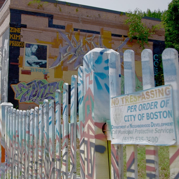 graffitied building and white picket fence with a sign stating "no trespassing per order of city of Boston."
