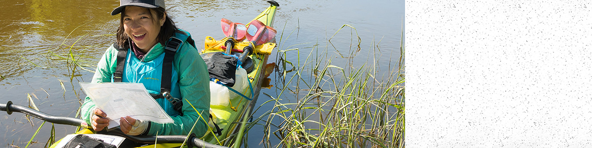 Student holds a paper chart while on the water in a kayak filled with water sampling supplies.
