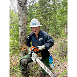 smiling student with hard hat and chain saw in a forest