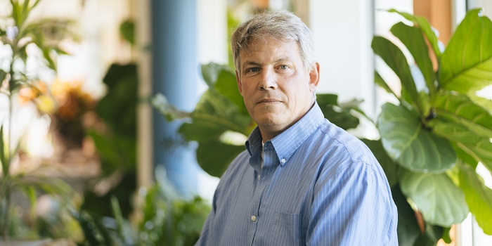Allan Strong sitting in the Aiken Solarium in front of indoor greenery