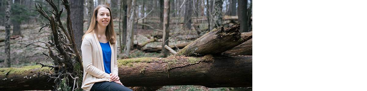 Mariah Choiniere sits on log in forest.
