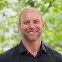 James Sullivan smiles while standing in front of greenery outside