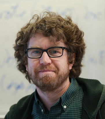 Headshot of Gregory Rowangould. He is smiling in front of greenery outdoors