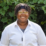 Elyse standing in front of dark green leaves wearing a white shirt and smiling