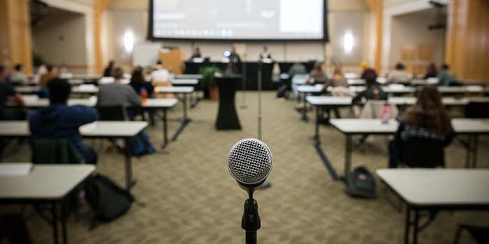 a meeting happening in a ballroom with tables and a microphone