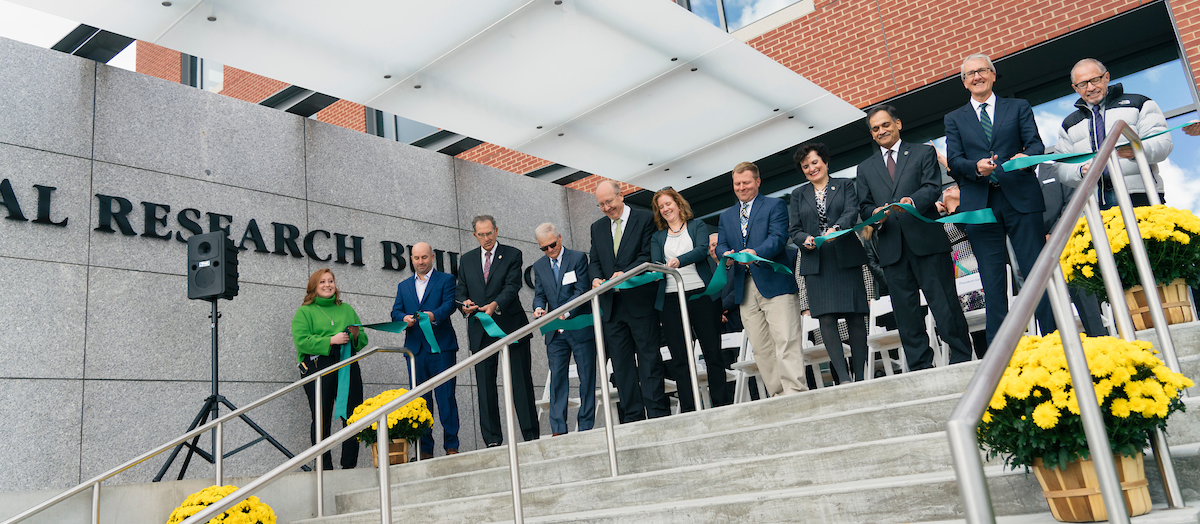 A row of people holds a green ribbon, ready to cut it to open a new building