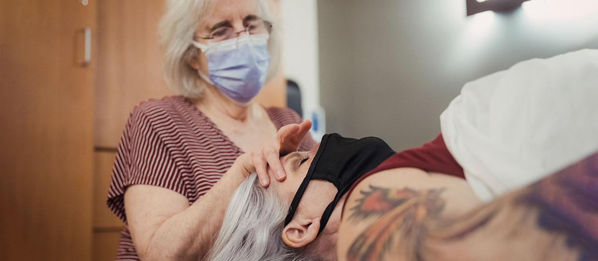 A patient lays down while a practitioner lays a hand on her forehead