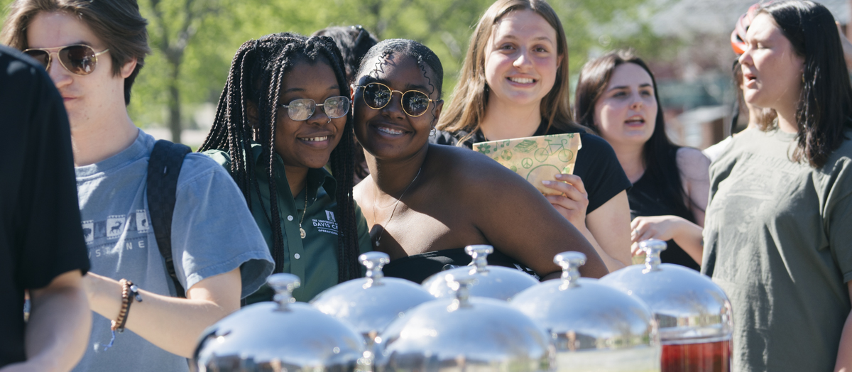 Students smile while in line for food on the green