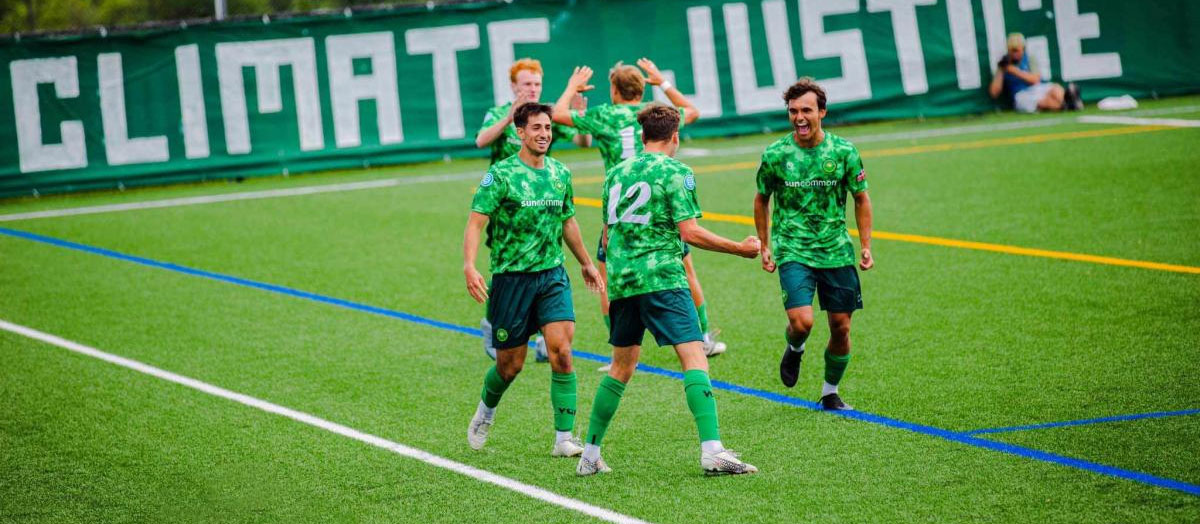Soccer players in green jerseys celebrate on the field after a goal