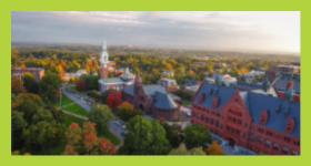 Aerial view of green and orange trees throughout campus filled with red stone building and white tower in the distance.