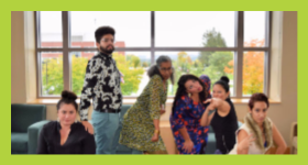 Group of people posing making silly faces, in front of large windows.