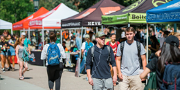 multiple students walk down a sidewalk lined with tents for numerous clubs and organizations