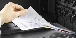 A hand retrieves a stack of papers fresh off the printer