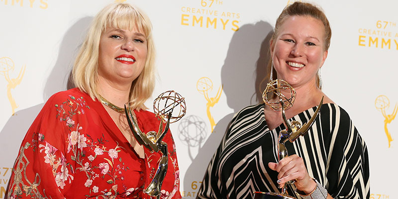 Two women holding Emmy Awards, Marie Schley '94 on the left wearing a bright red floral dress and blonde shoulder length hair with bangs.