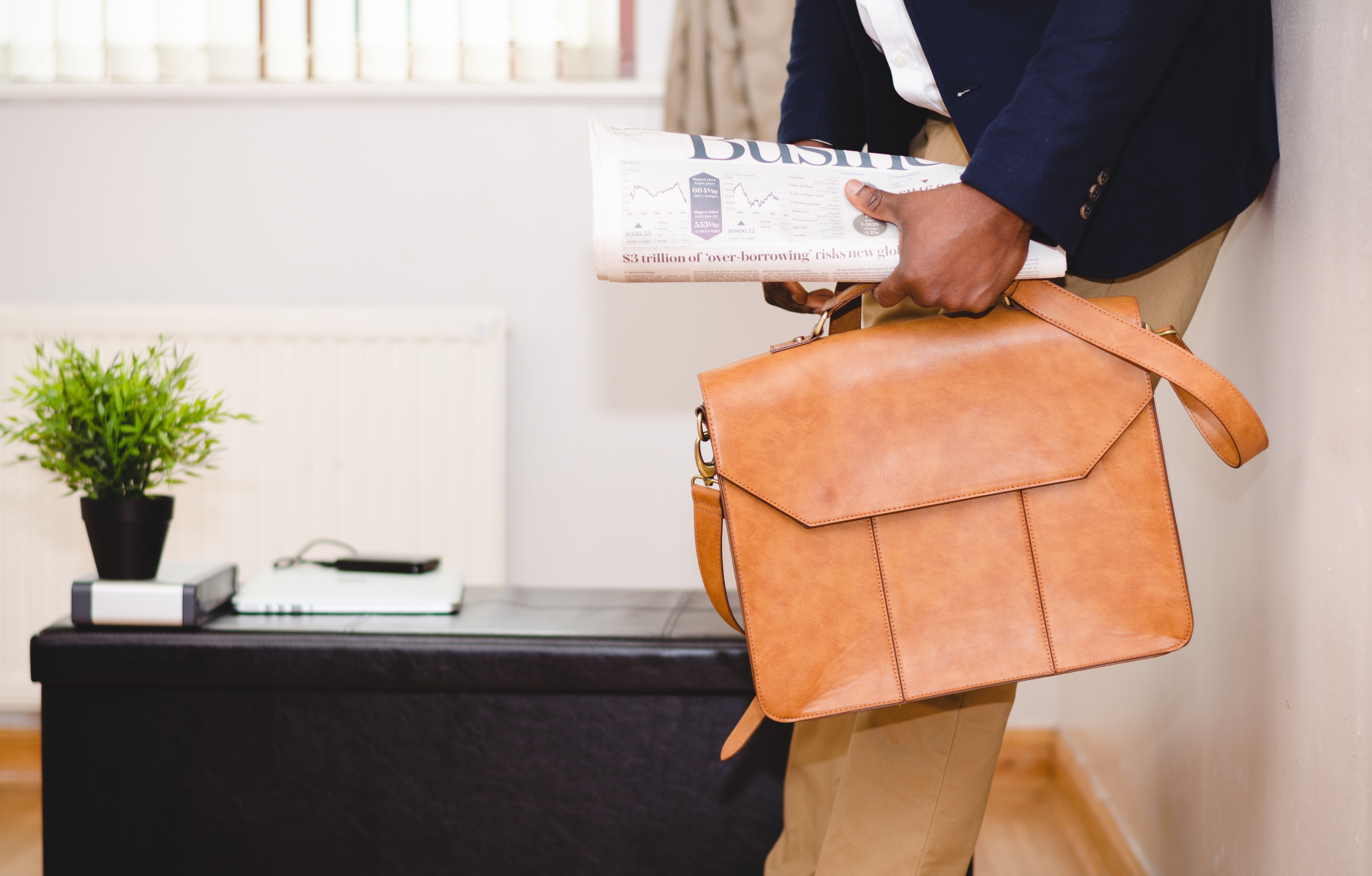 Person standing in an office holding a brown satchel and newspaper.