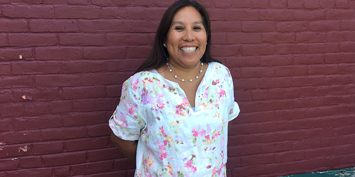 Mary H Mary is standiing by a wall and is smiling in a white shirt