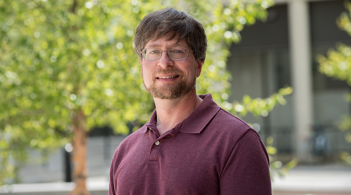 David Feurzeig smiling outdoors with campus greenery in the background