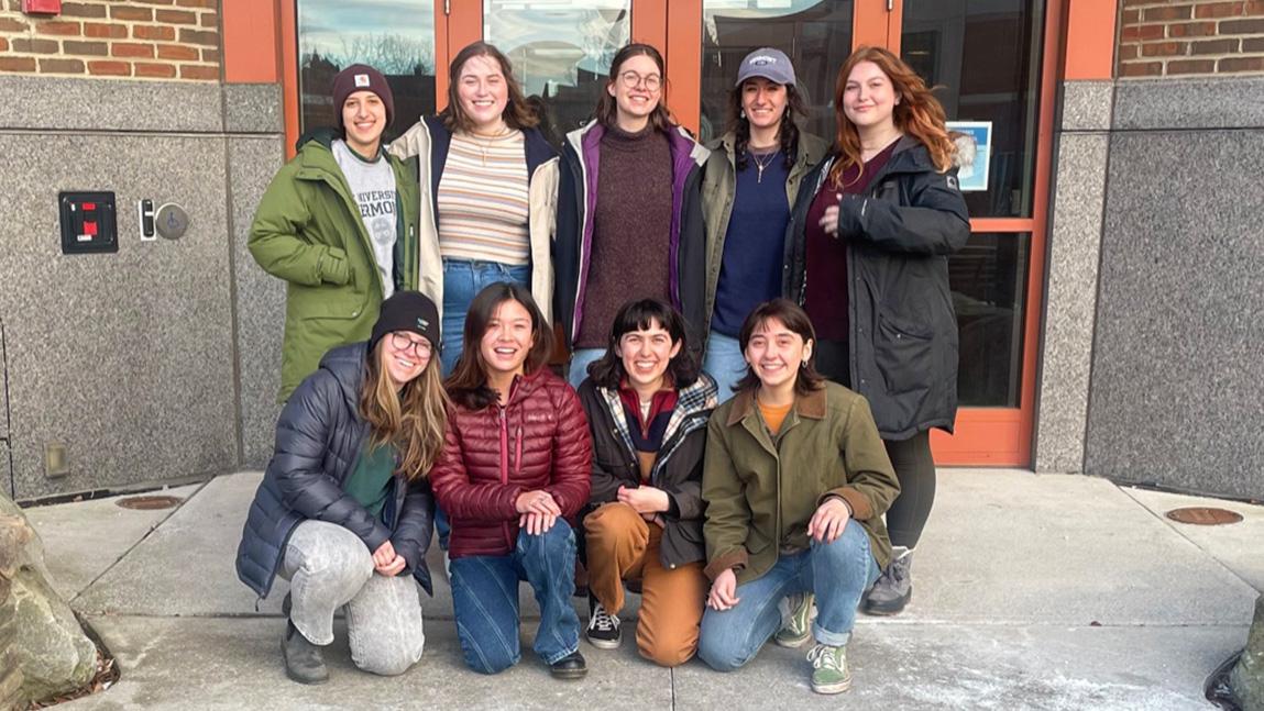 Eight female-identifying natural resource students pose in 2 rows in front of campus building