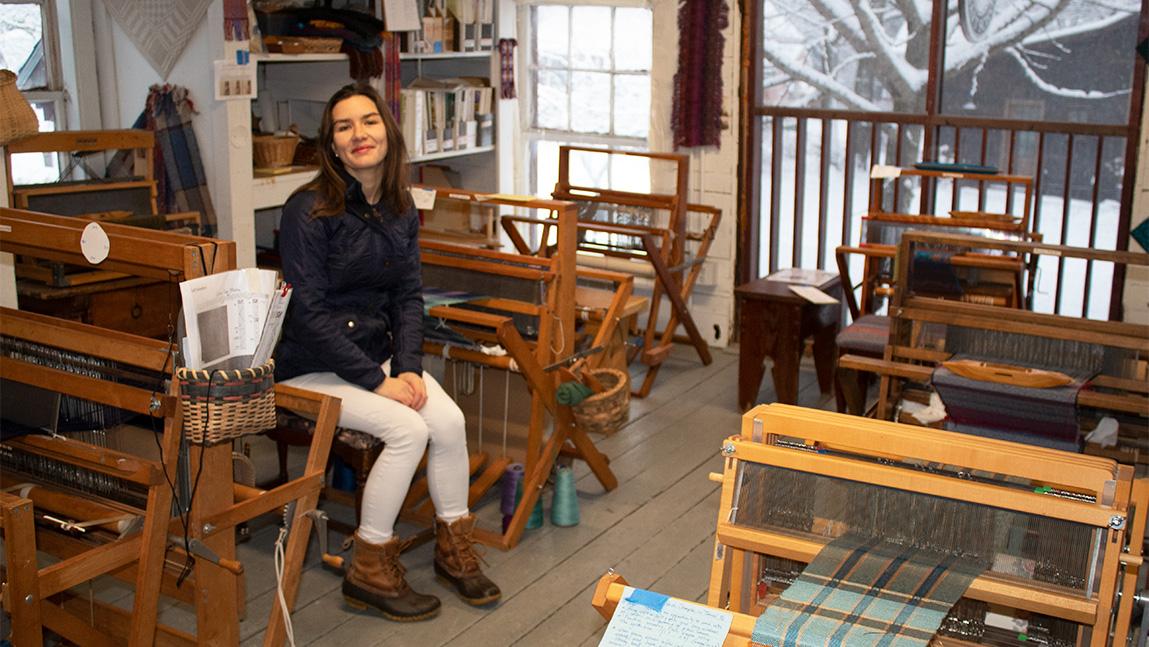 Smiling person in a sun filled room with wool fiber and looms