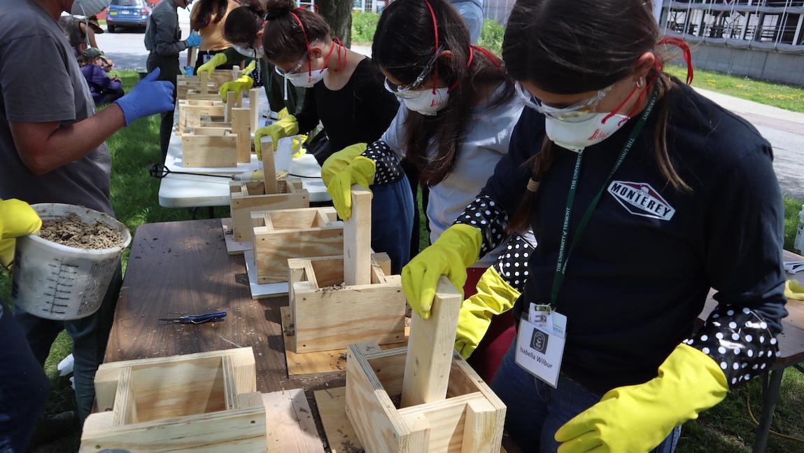 a group of students wearing personal protective gear using wooden blocks to create hempcrete during an outdoor lab at UVM.