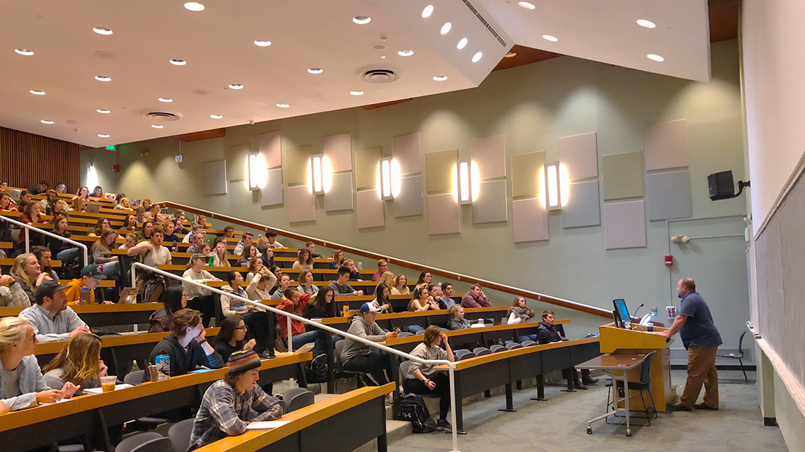 Erik Ruggles at a podium in a large lecture hall