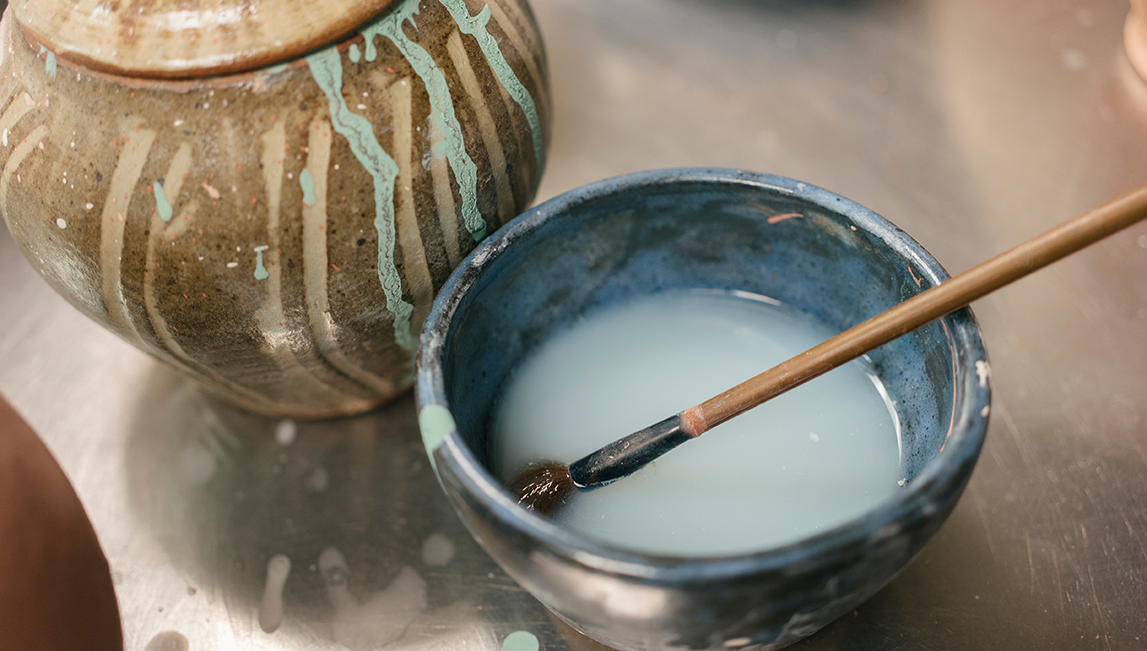 two earthen bowls of different colors with glaze material and brush