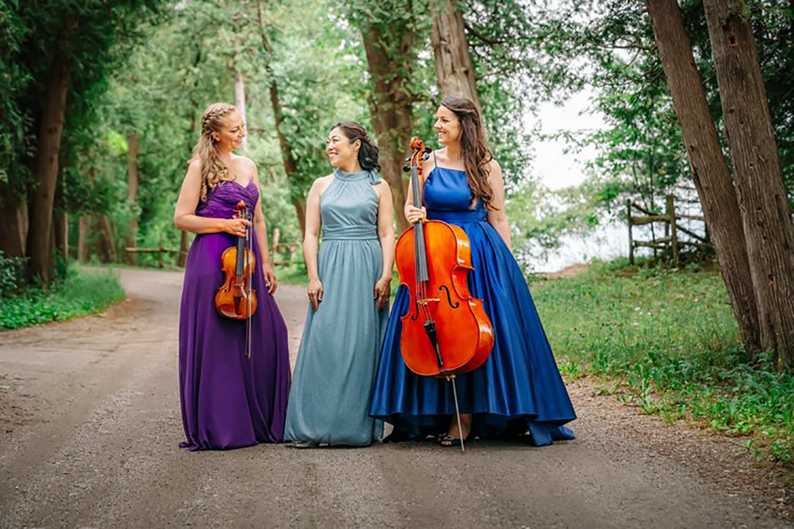 Ladies of the trio dressed to the nines on a dirt road with green trees in the backgroun