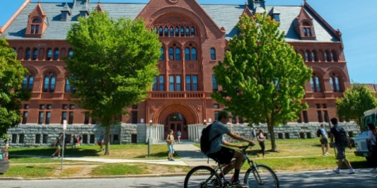 Red stone building in background, man riding bike in the foreground.