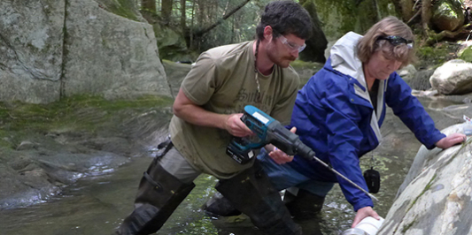 Grduate students installing a suspended sediment sampling device in a river channel