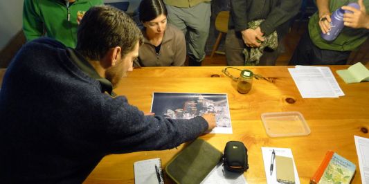 A man points at a map on a table with others gathered around