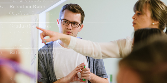 Professor teaching at the white board while student actively listens