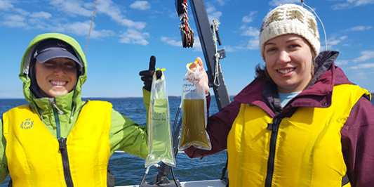 Two students on boat holding water sample bags