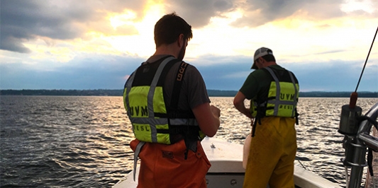 Two students work in boat on lake at sunset