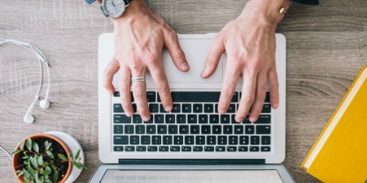 Hands typing on a laptop, on a desk.