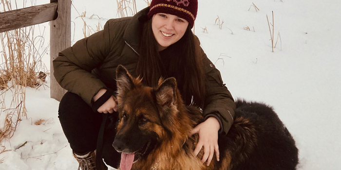Julia Kitonis dressed for Winter with a snowy backdrop and german shepard type dog companion