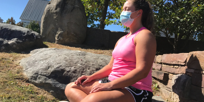 Person meditating outdoors, wearing a face mask, a pink tank top and black shorts