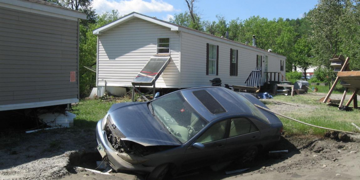 damaged car washed up in the yard of a mobile home resident with more storm debris in the background.